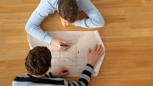 an overhead photos of two people looking at a technical drawing that is spread out between them